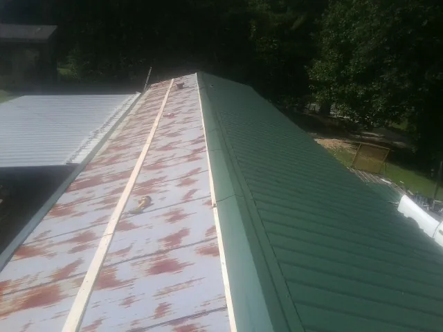 Old rusted panels beside newly installed green metal roofing — Wind Damage Roof Repair by Roofing Brothers in Le Roy