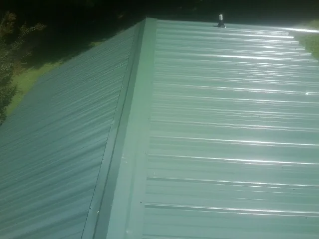 New green metal panels meeting at the ridge of a roof — Flat Roof Repair work by our crew in Le Roy