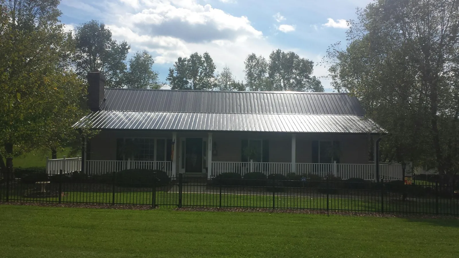 Gray metal roof on a brick ranch with a full width front porch — Gutter Guard Installation work by our crew in Le Roy