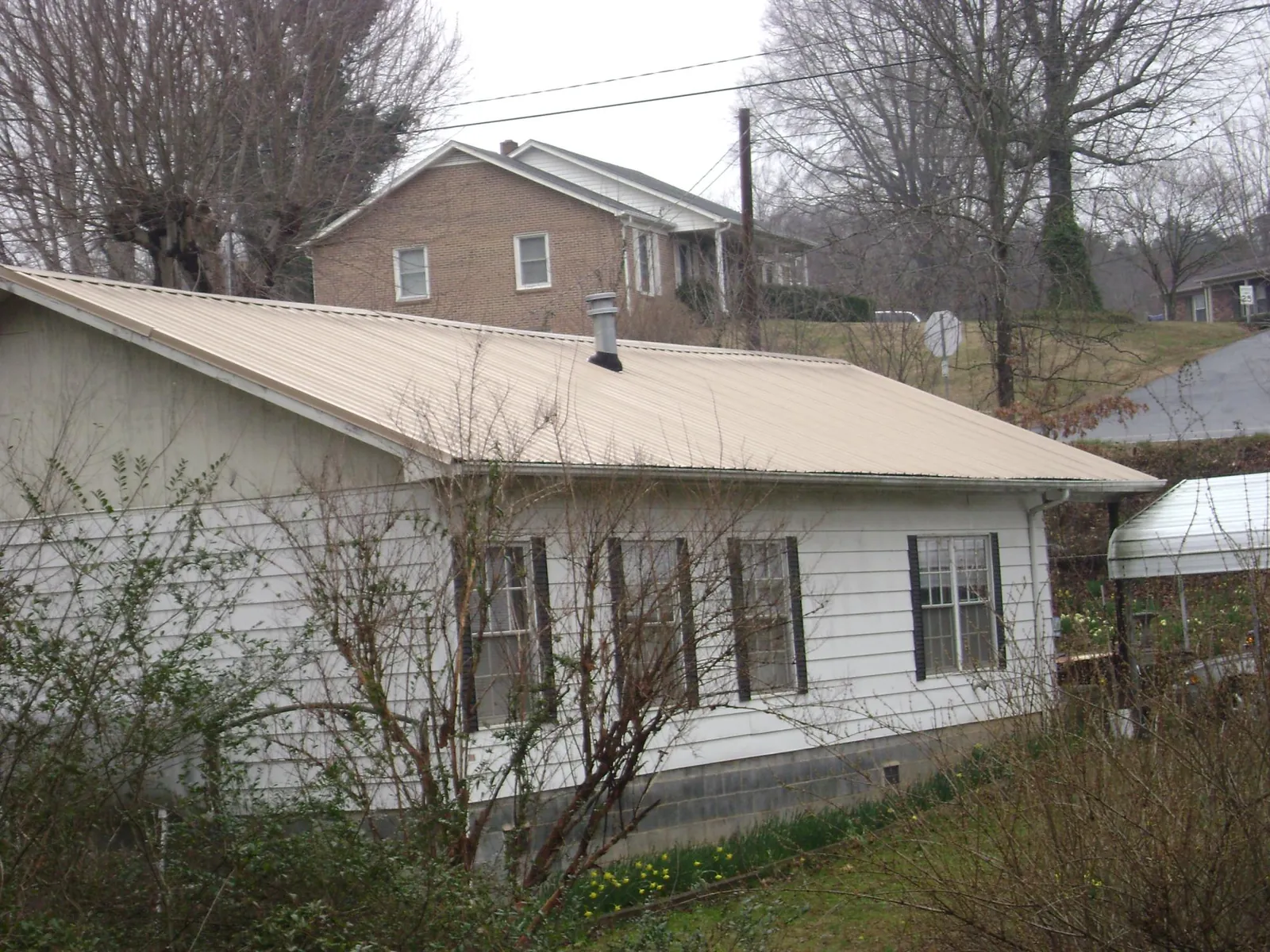 Tan metal roof on a white sided house set into a hillside — Commercial Roofing by Roofing Brothers in Le Roy